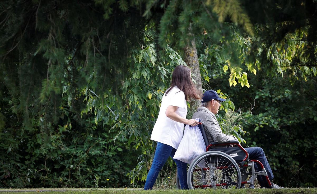 Una mujer pasea con un hombre en silla de ruedas junto a una residencia en San Sebastián. Foto: EFE